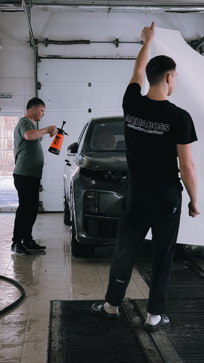 Two technicians detailing a car in an indoor garage, showcasing professional car care service.